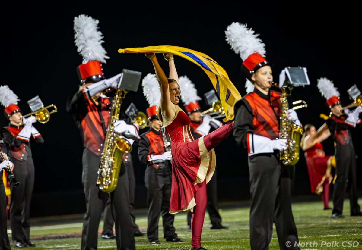 The marching band along with a color guard member performing during a home halftime show. Picture from the North Polk Flickr page.